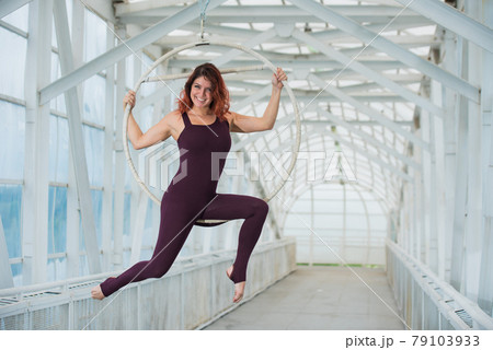 The red-haired aerial gymnast in a sports combo performs at the air hoop in a pedestrian crossing. The red-haired aerial gymnast in a sports combo performs at the air hoop in a pedestrian crossing. 79103933