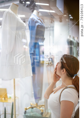Caucasian woman looking at a shop window and dreaming about a dress. 79106413