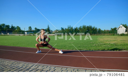 Young woman practicing side lunges at stadium. 79106481