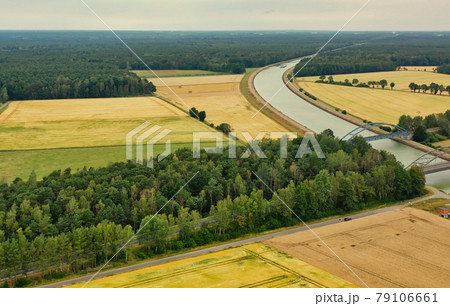 Aerial view of a canal that runs through fields, meadows and arable land in the flat landscape of northern Germany. 79106661