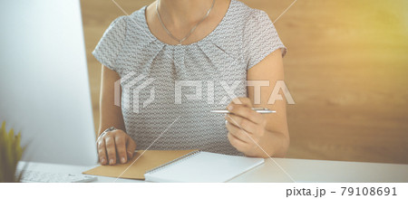 Unknown business woman working with computer while sitting at the desk in sunny office, close-up. Middle aged female lawyer at work 79108691