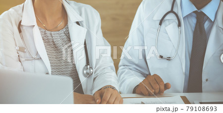 Two unknown doctors discussing treatment problems while sitting at the desk in sunny hospital office, close-up 79108693
