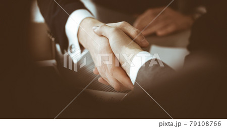 Unknown businessman shaking hands with his colleague or partner above the glass desk in modern office, close-up. Business people group at meeting 79108766