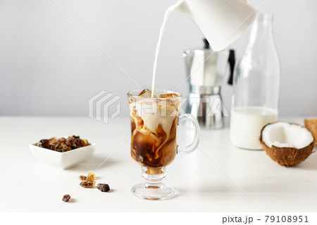 Pouring coconut milk into glass with iced coffee. 79108951