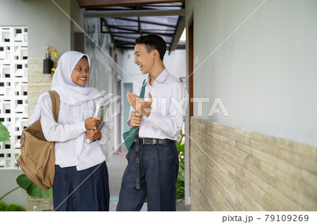 a male and female student in school uniform chatting together while carrying books 79109269