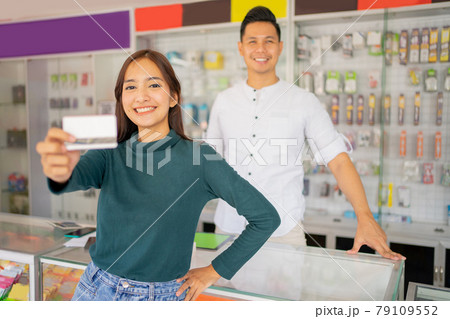 a female customer smiles while showing a credit card for cashless payment to the camera 79109552