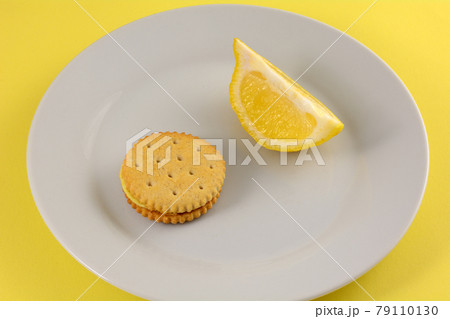 Lemon cream sandwich cookie with lemon slice on white snack plate with yellow background Lemon cream sandwich cookie with lemon slice on white snack plate with yellow background 79110130