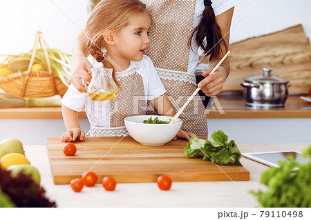 Happy woman and her daughter making healthy vegan salad and snacks for family feasting in sunny kitchen. Christmas, New year, Thanksgiving, Anniversary, Mothers Day. Healthy meal cooking concept Happy woman and her daughter making healthy vegan salad and snacks for family feasting in sunny kitchen. Christmas, New year, Thanksgiving, Anniversary, Mothers Day. Healthy meal cooking concept 79110498