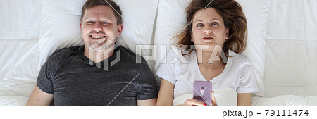 Young man and woman lying in bed and holding phone and joystick top view Young man and woman lying in bed and holding phone and joystick top view 79111474