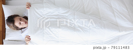 Woman in surprise looking under blanket in bed top view 79111483