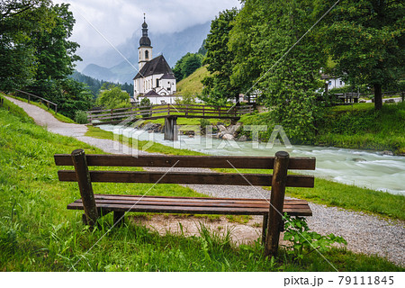 A wood bench with parish church, river abd mountains in background. berchtesgaden, Ramsau Germany A wood bench with parish church, river abd mountains in background. berchtesgaden, Ramsau Germany 79111845