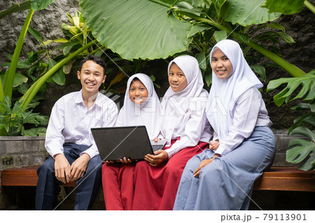 four teenagers in school uniforms smile while sitting using a laptop four teenagers in school uniforms smile while sitting using a laptop 79113901