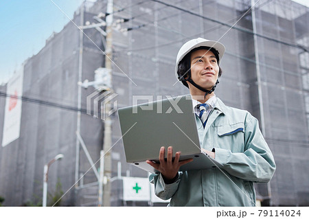建設現場の前でパソコンを見る作業服の男性 79114024