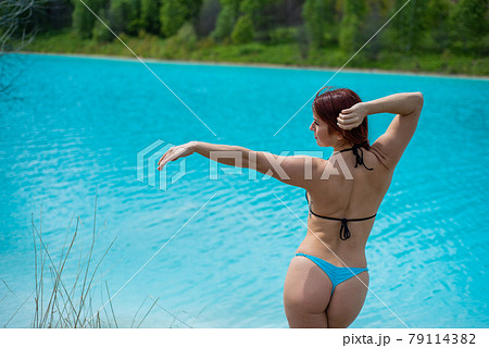 A beautiful red-haired woman in a blue seductive bikini stands with her back against an unusual turquoise lake. A miracle of nature, bright blue clear water. Maldives. Ash dump, poisoned water. A beautiful red-haired woman in a blue seductive bikini stands with her back against an unusual turquoise lake. A miracle of nature, bright blue clear water. Maldives. Ash dump, poisoned water. 79114382