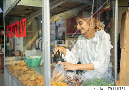 a beautiful girl wearing a hijab while using tongs chooses fried food the buyer orders a beautiful girl wearing a hijab while using tongs chooses fried food the buyer orders 79116571