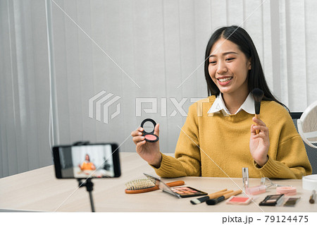 Young asian woman vlogging about cosmetics skin care items products on table with her video camera and demonstrates product use and reviews for her online blog channel. Young asian woman vlogging about cosmetics skin care items products on table with her video camera and demonstrates product use and reviews for her online blog channel. 79124475