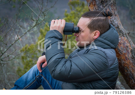 Traveler with monocle sitting on a large branch of conifer and looks into the distance. Traveler with monocle sitting on a large branch of conifer and looks into the distance. 79126386