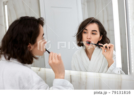 woman in white bathrobes brushing teeth in front of mirror woman in white bathrobes brushing teeth in front of mirror 79131816