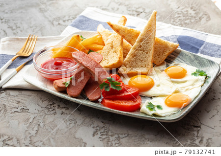 English breakfast with eggs, sausages, french toasts and potato wedges on gray table 79132741