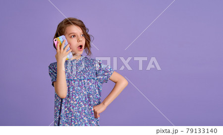 Surprized little girl holding telephone with open mouth isolated over violet color background Surprized little girl holding telephone with open mouth isolated over violet color background 79133140
