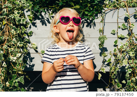 Happy carefree emotional child in summer sunglasses shows tongue and grimaces. Happy carefree emotional child in summer sunglasses shows tongue and grimaces. 79137450