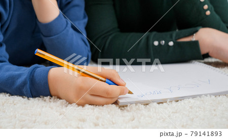Closeup of little boy writing with pen in copybook while lying on carpet in living room. Concept of child education, development Closeup of little boy writing with pen in copybook while lying on carpet in living room. Concept of child education, development 79141893