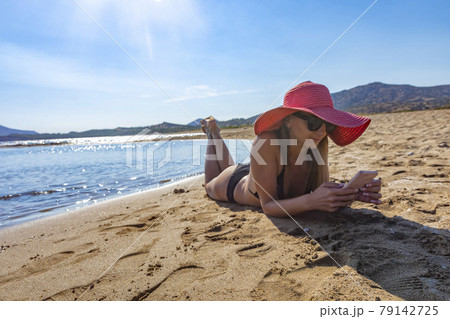 woman in black bikini and red hat lying on tropical beach 79142725