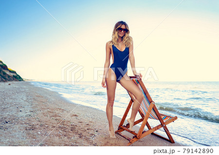 A young woman in a swimsuit relaxing on a deckchair on the beach A young woman in a swimsuit relaxing on a deckchair on the beach 79142890