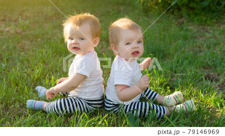 The twins are sitting on the green grass on a sunny day in the city park The twins are sitting on the green grass on a sunny day in the city park 79146969