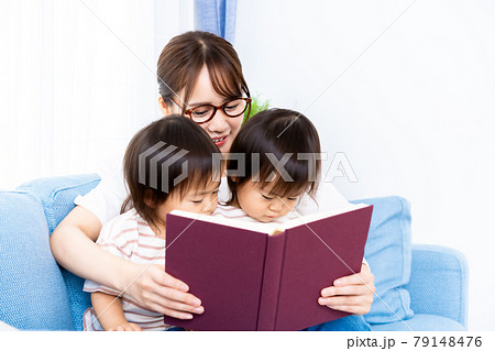 ソファで本を読む双子の女の子とママの写真素材