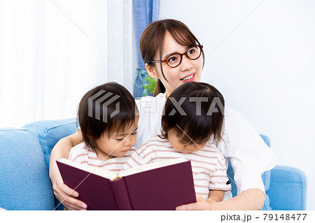 ソファで本を読む双子の女の子とママの写真素材