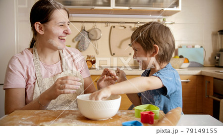 Laughing mother with son throwing flour at each other while cooking at home. Children cooking with parents, little chef, family having time together, domestic kitchen. 79149155