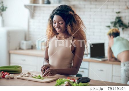 Dark-skinned woman chopping vegetables and girlfriend at distance Dark-skinned woman chopping vegetables and girlfriend at distance 79149194