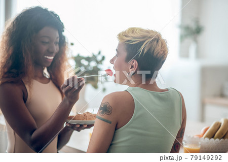 Dark-skinned woman feeding caucasian girlfriend with tomato Dark-skinned woman feeding caucasian girlfriend with tomato 79149292