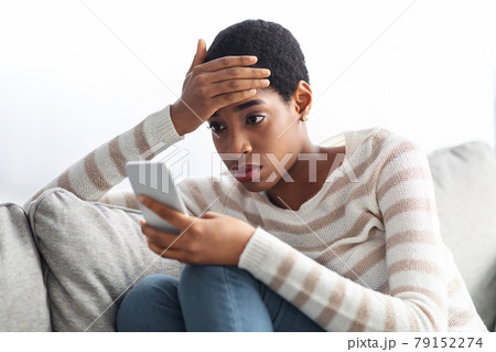 Concerned Black Lady Looking At Smartphone Screen At Home And Touching Head 79152274