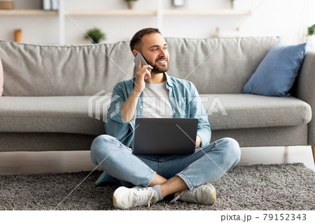 Full length of happy young guy using laptop and mobile phone at home, having freelance job 79152343