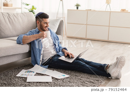 Smiling jewish man watching video on pc, drinking hot coffee Smiling jewish man watching video on pc, drinking hot coffee 79152464