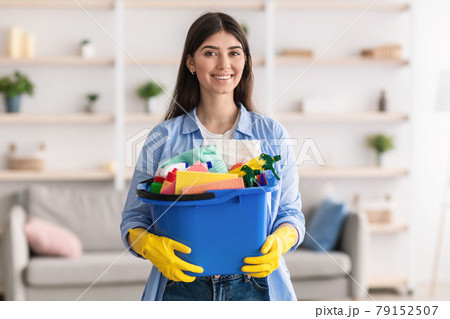 Cheerful young housewife holding bucket with cleaning supplies tools 79152507