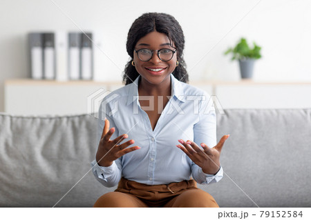 Portrait of smiling young black psychologist gesturing and smiling at camera, sitting on comfy couch at modern office Portrait of smiling young black psychologist gesturing and smiling at camera, sitting on comfy couch at modern office 79152584