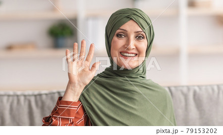 Happy Mature Muslim Lady In Hijab Waving Hand At Home 79153202