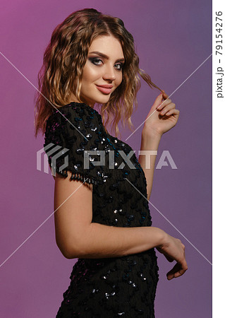 Elegant brown-haired lady with curly hair, bright make-up, in black shiny dress is posing against colorful background. Fashion and beauty. Close-up. 79154276