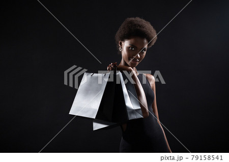 Black Friday concept. African american woman hold black shopping bags on black background. 79158541