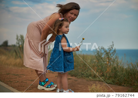 Woman and child stand in a meadow overlooking the sea Woman and child stand in a meadow overlooking the sea 79162744