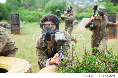 Excited male and female paintball players in protective uniform aiming and shooting with guns outdoor Excited male and female paintball players in protective uniform aiming and shooting with guns outdoor 79168029