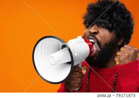 Young african american man in red hoodie screaming in megaphone against yellow background Young african american man in red hoodie screaming in megaphone against yellow background 79171873