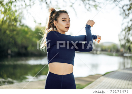Fit young girl in dark blue sportswear exercising in park 79172475