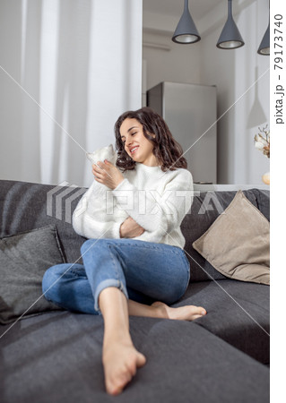 Cute young woman sitting on the sofa and hugging her cat 79173740