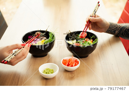 Loving couple man and woman eating salad poke chopsticks. Place the tuna salad in a bowl. People in Loving couple man and woman eating salad poke chopsticks. Place the tuna salad in a bowl. People in 79177467