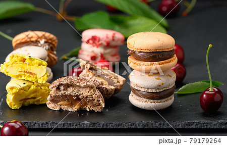 stack of multicolored macarons and ripe red cherries on black wooden background 79179264