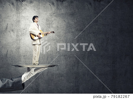 Businessman on metal tray playing acoustic guitar against concrete wall background Businessman on metal tray playing acoustic guitar against concrete wall background 79182267